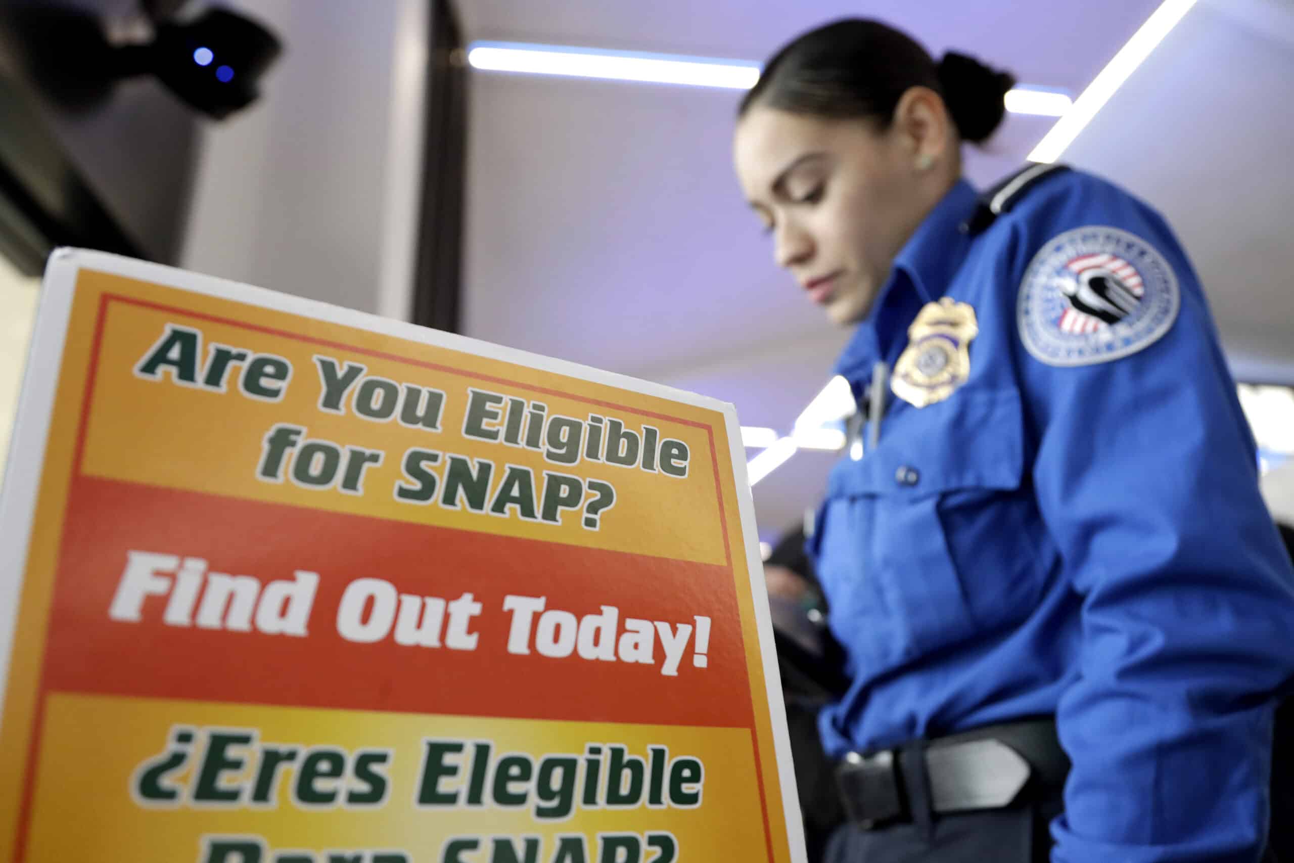 A Transportation Security Administration employee stands at a booth to learn about a food stamp program at a food drive at Newark Liberty International Airport, Wednesday, Jan. 23, 2019, in Newark, N.J. TSA employees each received a box of non perishables and a bag of produce to help them during the shutdown. (AP Photo/Julio Cortez)