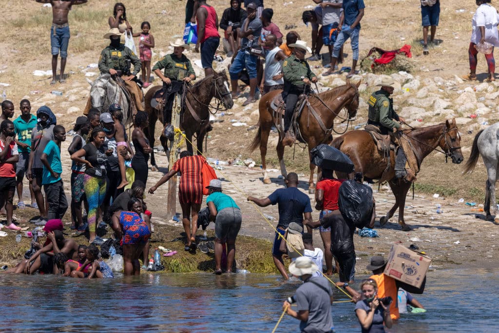 CIUDAD ACUNA, MEXICO - SEPTEMBER 20: Mounted U.S. Border Patrol agents watch Haitian immigrants on the bank of the Rio Grande in Del Rio, Texas on September 20, 2021 as seen from Ciudad Acuna, Mexico. As U.S. immigration authorities began deporting immigrants back to Haiti from Del Rio, thousands more waited in a camp under an international bridge in Del Rio while others crossed the river back into Mexico to avoid deportation. (Photo by John Moore/Getty Images)