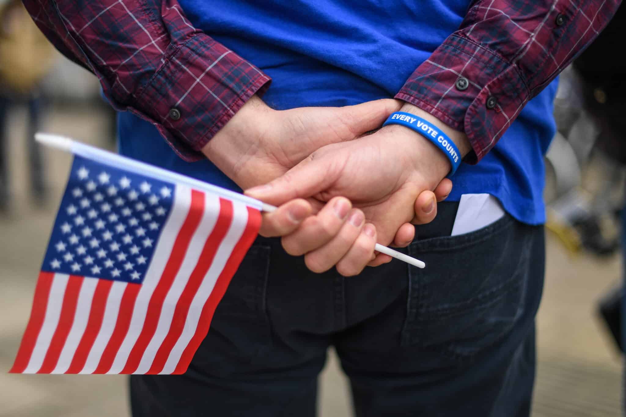 OXFORD, ENGLAND - MARCH 03: A man holds an American flag while wearing a wristband reading 'Every Vote Counts' outside a polling station on 'Super Tuesday' on March 3, 2020 in Oxford, England. 1,357 Democratic delegates are at stake as voters cast their ballots in 14 states and American Samoa on what is known as Super Tuesday. (Photo by Peter Summers/Getty Images)