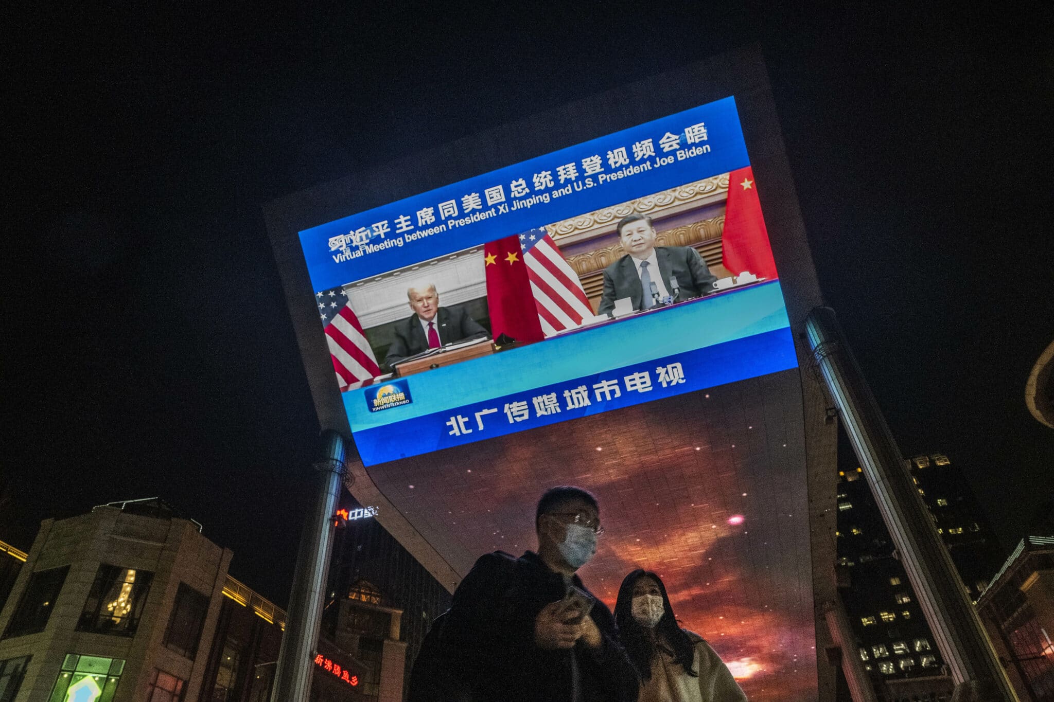 BEIJING, CHINA - NOVEMBER 16: A large screen displays United States President Joe Biden, left, and China's President Xi Jinping during a virtual summit as people walk by during the evening CCTV news broadcast outside a shopping mall on November 16, 2021 in Beijing, China. The two leaders met for more than three hours and discussed trade, climate change, Taiwan and other issues in what was their longest meeting since Biden was elected last year. (Photo by Kevin Frayer/Getty Images)