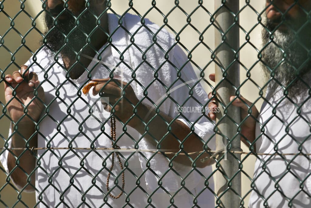 FILE - In this photo, reviewed by a US Department of Defense official, detainees stand together at a fence, one holding Islamic prayer beads, at Camp Delta prison, at the Guantanamo Bay U.S. Naval Base, Cuba, on Tuesday, Sept. 19, 2006. A 74-year-old from Pakistan who was the oldest prisoner at the Guantanamo Bay detention center was released and returned to Pakistan on Saturday,  the foreign ministry in Islamabad said Saturday, Oct. 29, 2022.  (AP Photo/Brennan Linsley, File)