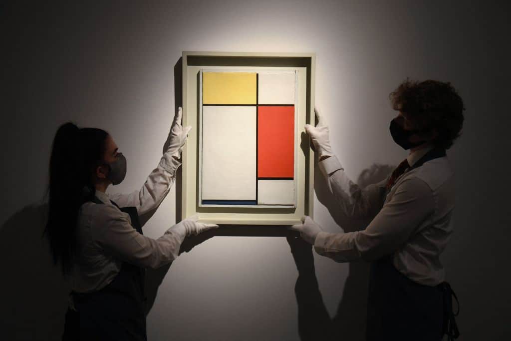 Gallery workers display an artwork titled 'Composition: No. II, with Yellow, Red and Blue' by Dutch painter Piet Mondrian during a photocall at Christies auction house in central London on April 22, 2021. - RESTRICTED TO EDITORIAL USE - MANDATORY MENTION OF THE ARTIST UPON PUBLICATION - TO ILLUSTRATE THE EVENT AS SPECIFIED IN THE CAPTION (Photo by Daniel LEAL / AFP) / RESTRICTED TO EDITORIAL USE - MANDATORY MENTION OF THE ARTIST UPON PUBLICATION - TO ILLUSTRATE THE EVENT AS SPECIFIED IN THE CAPTION / RESTRICTED TO EDITORIAL USE - MANDATORY MENTION OF THE ARTIST UPON PUBLICATION - TO ILLUSTRATE THE EVENT AS SPECIFIED IN THE CAPTION (Photo by DANIEL LEAL/AFP via Getty Images)