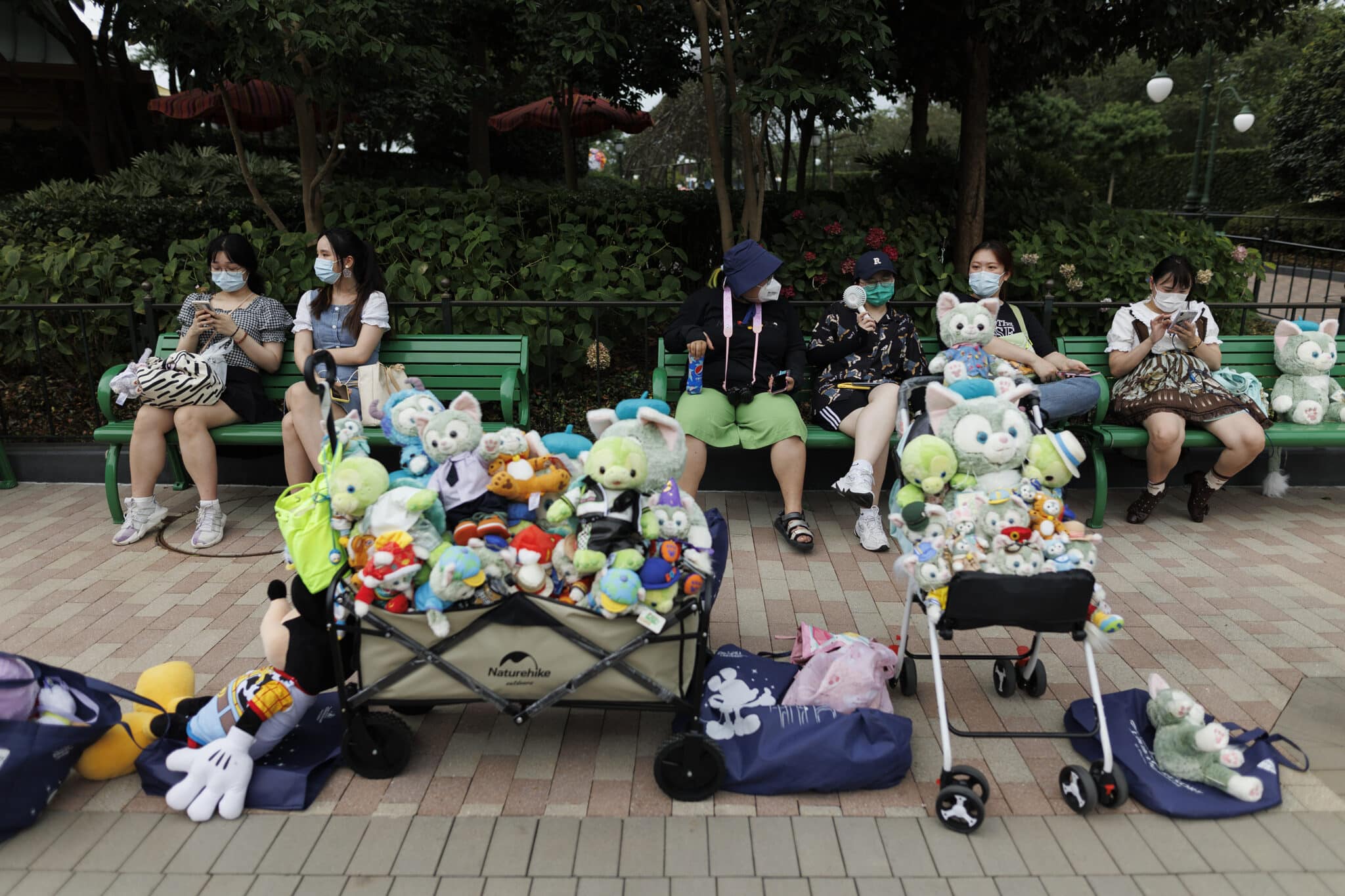 SHANGHAI, CHINA - JUNE 30: People rest behind carts of character plushies at Shanghai Disneyland on June 30, 2022 in Shanghai, China. (Photo by Hu Chengwei/Getty Images)