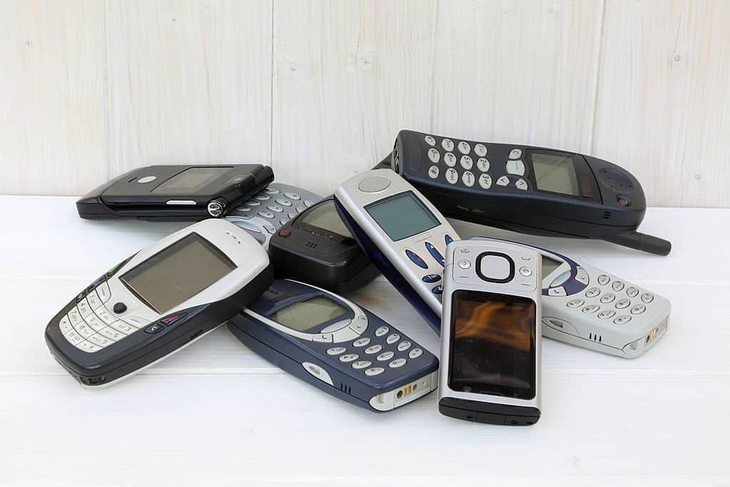 Nine outdated mobile phones stored in pile on shelf.