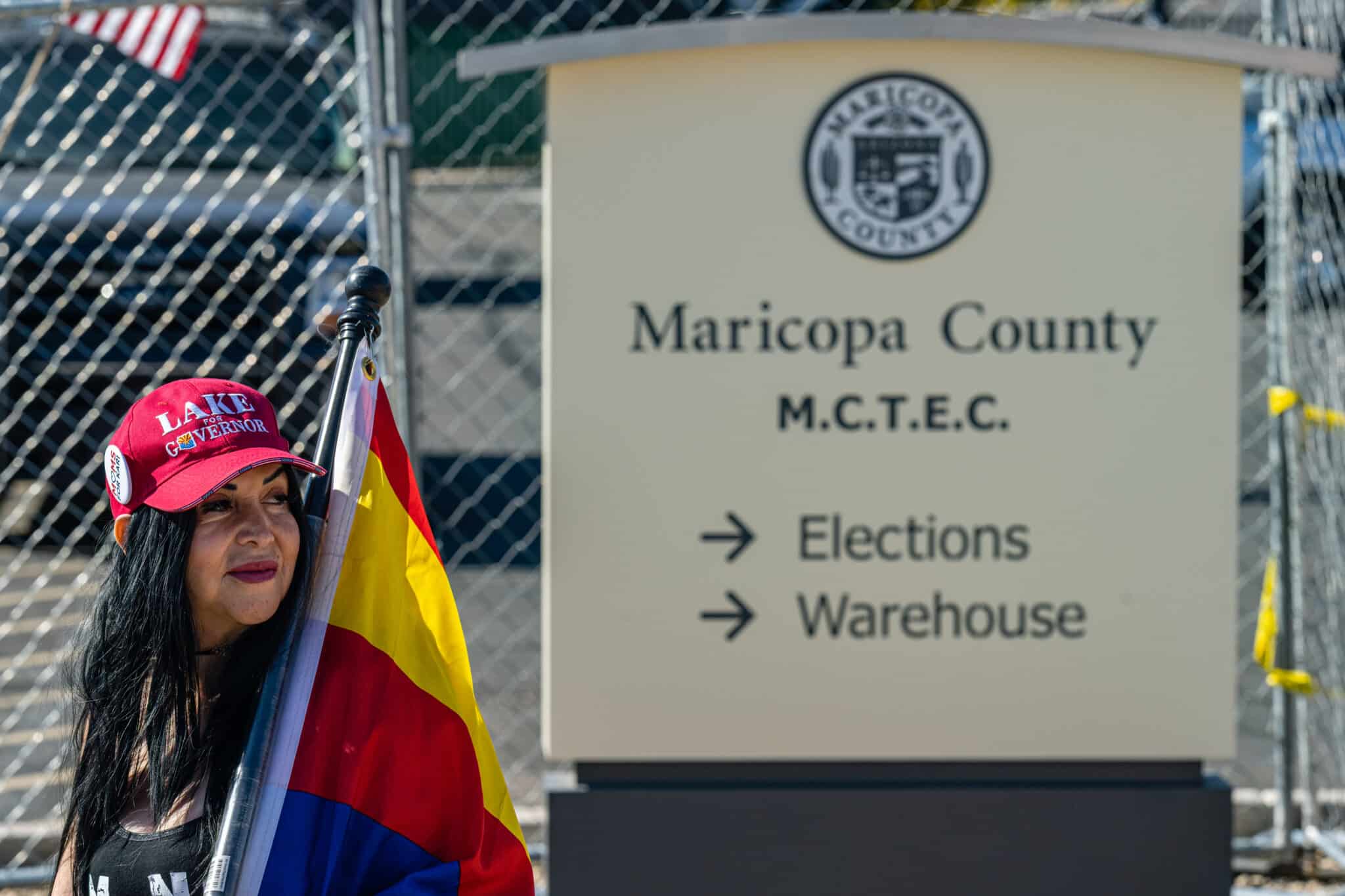 PHOENIX, AZ - NOVEMBER 14: A right wing activist wearing a 'LAKE FOR GOVERNOR' hat stands on the sidewalk in protest of the election process in front of the Maricopa County Tabulation and Election Center on November 14, 2022 in Phoenix, Arizona. Ballots continue to be counted in Maricopa County following the November 8 midterm election as officials push back against conspiracy theories claiming the process is being delayed. (Photo by Jon Cherry/Getty Images)