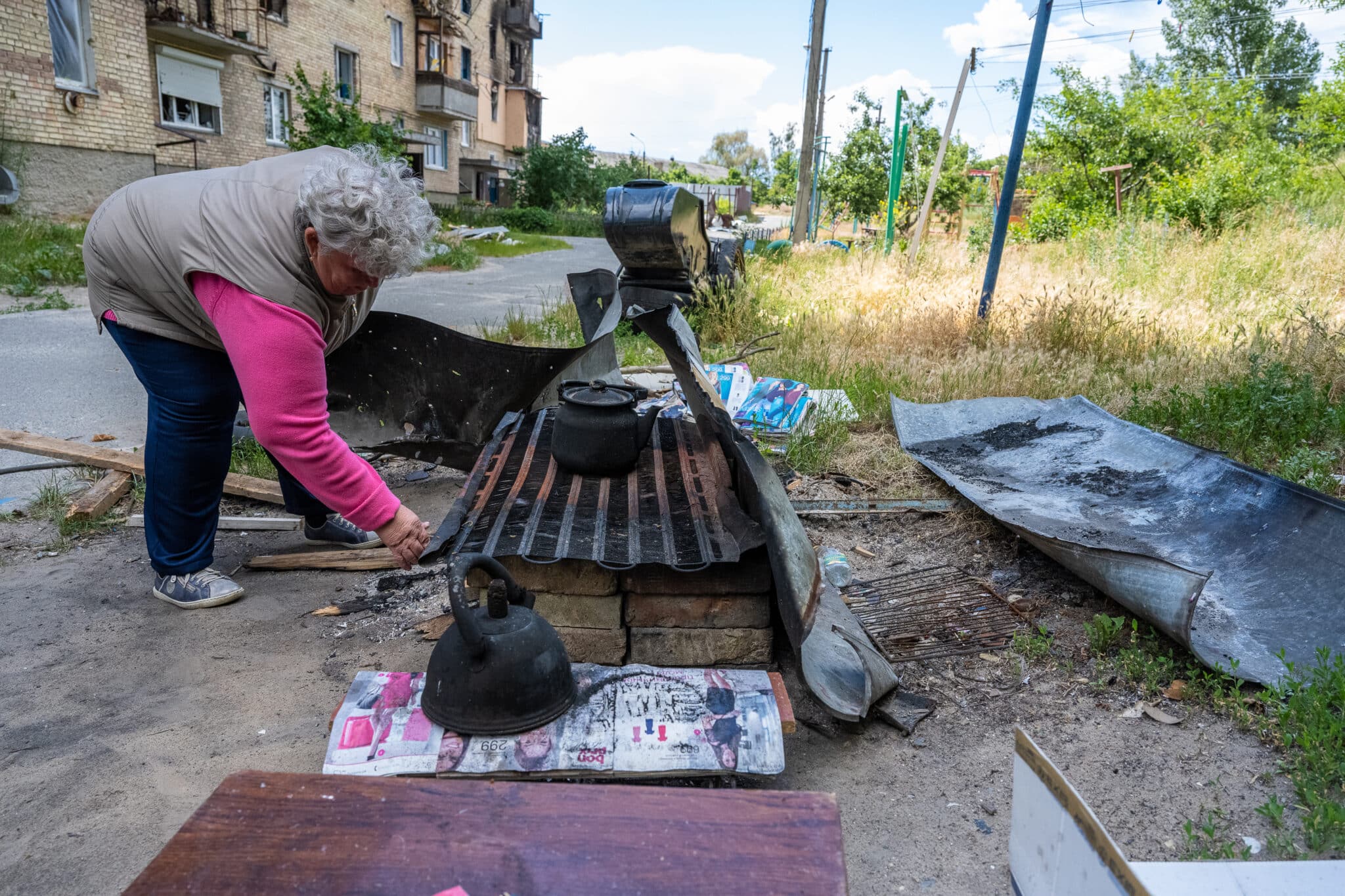 HORENKA, UKRAINE - JUNE 22: Ukrainian Olena Kalinovych moves blackened kettles on a makeshift outdoor stove used for cooking by remaining residents of an apartment block heavily damaged by a Russian rocket in early March, as they consider next steps to rebuild in the northern Kyiv suburb of Horenka, Ukraine, on June 22, 2022. Russian forces invading Ukraine on February 24 fought pitched battles with Ukrainian armed forces in the northern suburbs of the Ukrainian capital throughout March, leaving a trail of destruction that residents only today are beginning to cope with, as they attempt initial rebuilding efforts. (Photo by Scott Peterson/Getty Images)