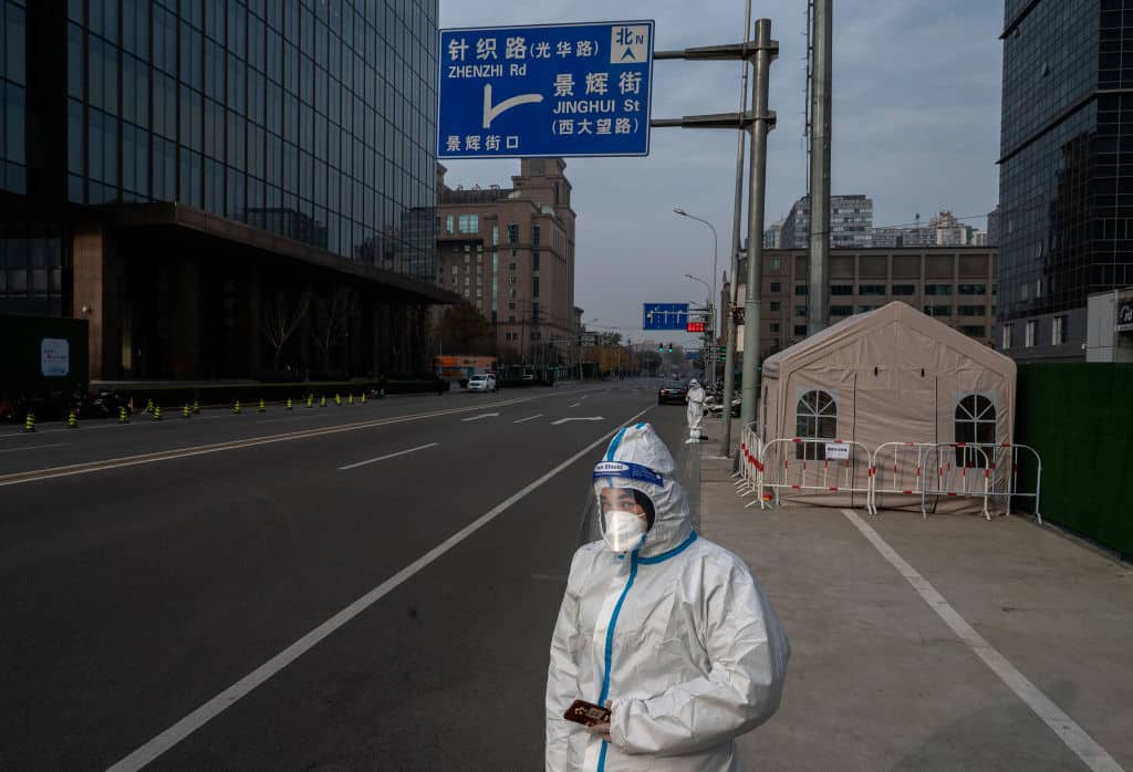 BEIJING, CHINA - NOVEMBER 23: An epidemic control worker wears protective clothing to protect against the spread of COVID-19 as she stands in a nearly empty street in the Central Business District on November 23, 2022 in Beijing, China. In an effort to try to bring rising cases under control, the local government last week closed most stores and restaurants for inside dining, switched  schools to online studies, and asked people to work from home. Though the government recently revised its COVID strategy, it has said it will continue to stick to its strict zero tolerance policy with mandatory testings, quarantines and lockdowns in many areas in an effort to control the spread of the virus. (Photo by Kevin Frayer/Getty Images)