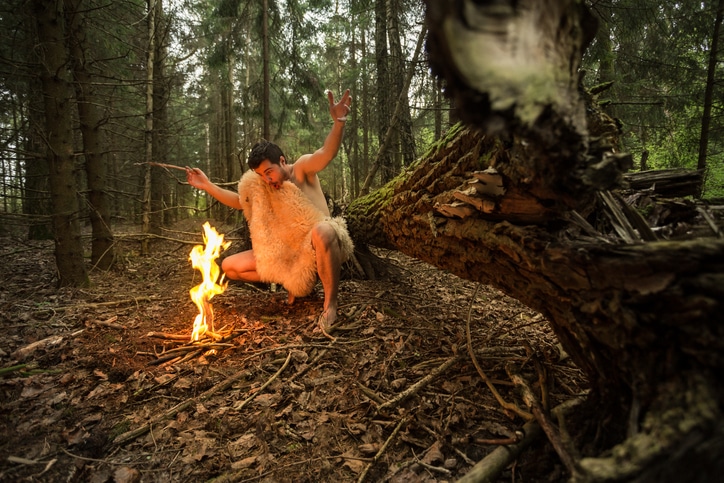 Caveman in animal skin kindles a fire in the forest