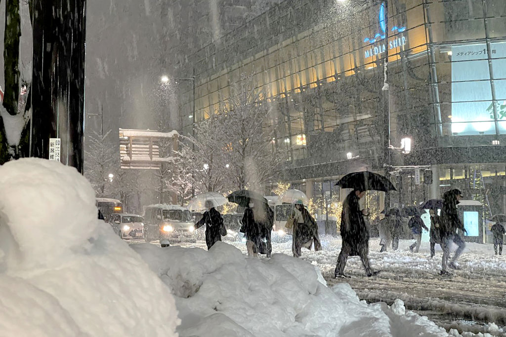 People cross the road carefully as heavy snow hits northern Japan in the city of Niigata on December 19, 2022. - Japan OUT (Photo by JIJI Press / AFP) / Japan OUT (Photo by STR/JIJI Press/AFP via Getty Images)