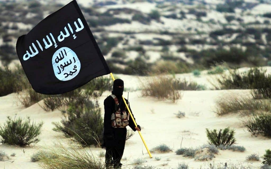 Islamic State/Iraq/Syria: A masked Islamic State soldier poses holding the ISIL banner somewhere in the deserts of Iraq or Syria. ISIL publicity image, 2015. (Photo by: Pictures from History/Universal Images Group via Getty Images)