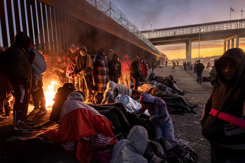 EL PASO, TEXAS - DECEMBER 22: Immigrants warm to a fire at dawn after spending the night outside next to the U.S.-Mexico border fence on December 22, 2022 in El Paso, Texas. A spike in the number of migrants seeking asylum in the United States has challenged local, state and federal authorities. The numbers are expected to increase as the fate of the Title 42 authority to expel migrants remains in limbo pending a Supreme Court decision expected after Christmas.  (Photo by John Moore/Getty Images)