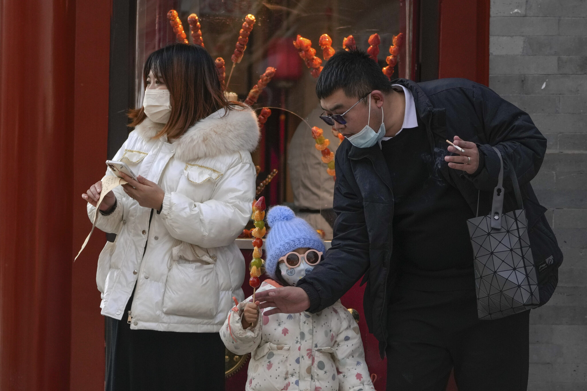 A couple buy a sugar-coated Chinese haw to a child at the Qianmen pedestrian shopping street, a popular tourist spot in Beijing, Tuesday, Jan. 3, 2023. As the virus continues to rip through China, global organizations and governments have called on the country start sharing data while others have criticized its current numbers as meaningless. (AP Photo/Andy Wong)