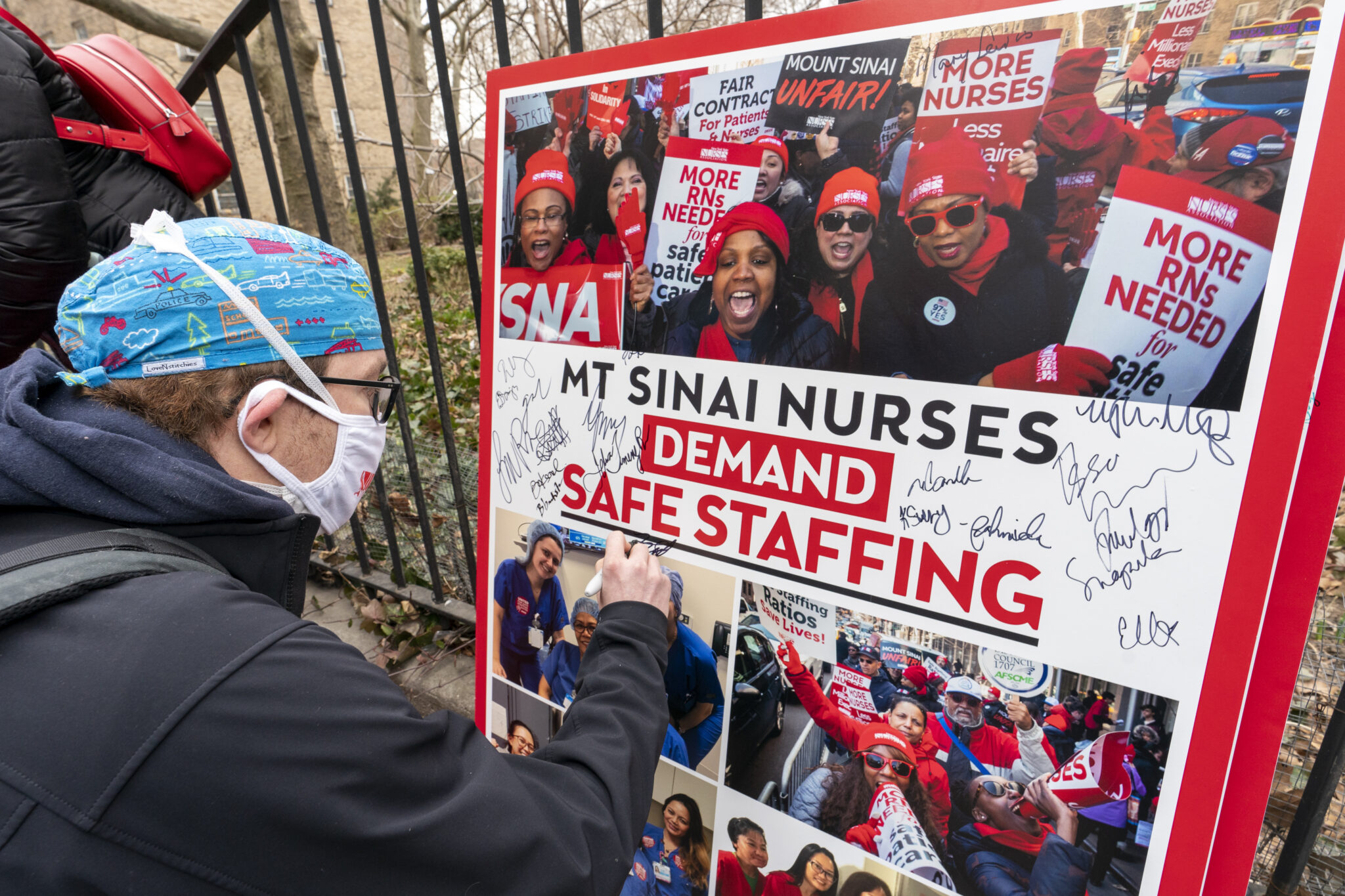 FILE - Zach Clapp, a nurse in the Pediatric Cardiac ICU at Mount Sinai Hospital signs a board demanding safe staffing during a rally by NYSNA nurses from NY Presbyterian and Mount Sinai, Tuesday, March 16, 2021, in New York. Negotiations to keep 10,000 New York City nurses from walking off the job headed Friday, Jna. 6, 2023, into a final weekend as some major hospitals braced for a potential strike by sending ambulances elsewhere and transferring such patients as vulnerable newborns.  (AP Photo/Mary Altaffer, File)