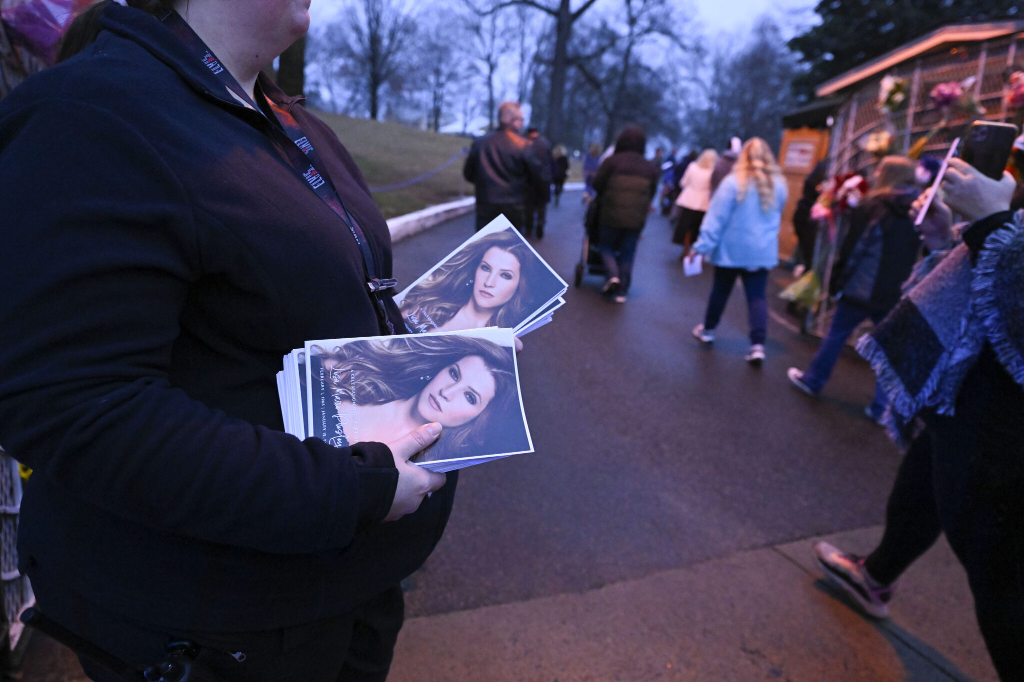 An attendant holds programs as fans enter Graceland for a memorial service for Lisa Marie Presley Sunday, Jan. 22, 2023, in Memphis, Tenn. She died Jan. 12 after being hospitalized for a medical emergency and was buried on the property next to her son Benjamin Keough, and near her father Elvis Presley and his two parents. (AP Photo/John Amis)